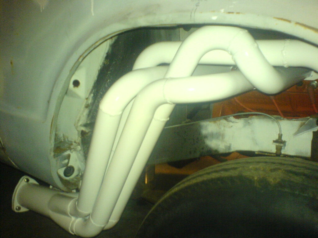White-painted tubular exhaust headers fitted in an engine bay