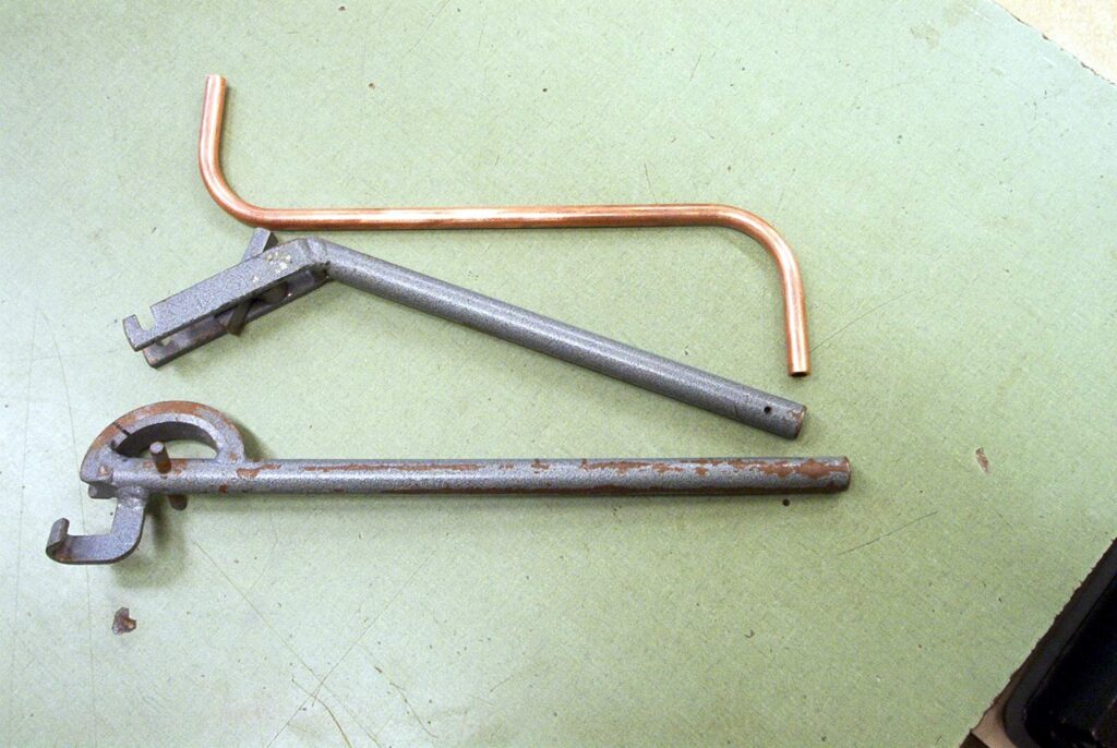 Pipe bending iron taken apart, next to a copper pipe bent at two corners