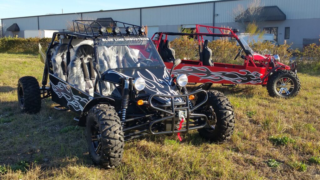 Two tube-frame sand rail buggies parked on grass outside a fabrication shop