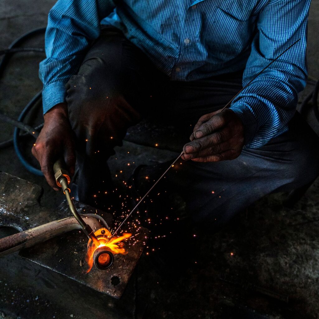 Welder's gloved hands working on a steel pipe with a gas torch, sparks flying